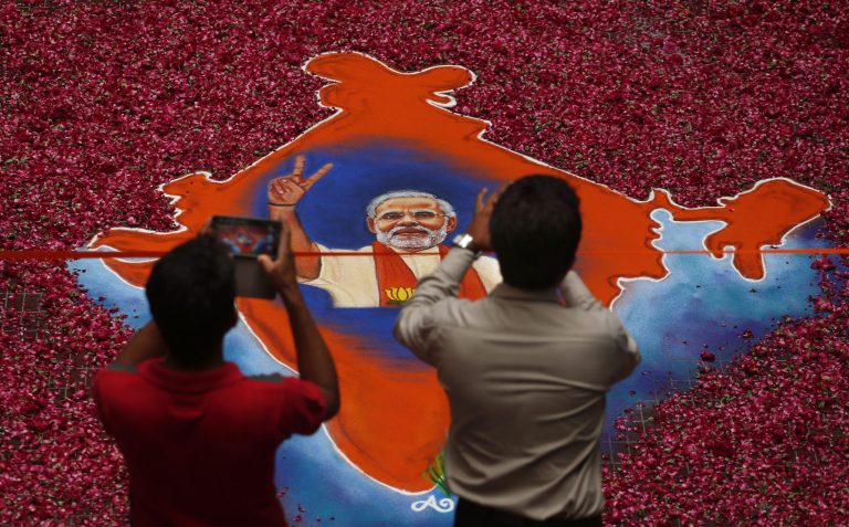 Indians take photographs of a map of India holding a portrait of the Bharatiya Janata Party (BJP) leader Narendra Modi, made with colored powder and surrounded by rose petals, at the party office in Gandhinagar, in the western Indian state of Gujarat, Friday, May 16, 2014. Modi will be India's next prime minister, winning the most decisive election victory the country has seen in more than a quarter century and sweeping the long-dominant Congress party from power, partial results showed Friday. (AP Photo/Saurabh Das)