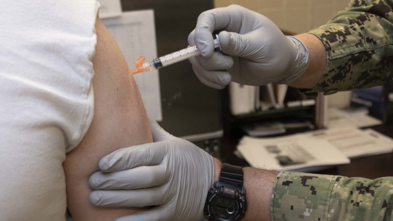 Hospital Corpsman 2nd Class Skyler Holt gives Personnel Specialist 1st Class Brian Raphael, a Defense Travel System Coordinator for selection board travel at Naval Personnel Command, a coronavirus vaccination.