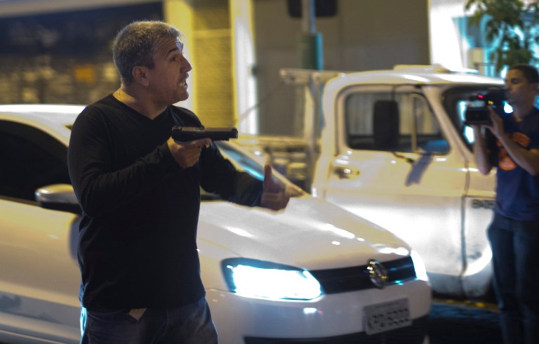 A man who identified himself as a police officer points his gun at anti-World Cup protesters blocking a road that leads to the Maracana stadium in Rio de Janeiro, Brazil, Sunday, June 15, 2014. The man told people not come any closer to him, and fired shots into the air which dispersed the crowd. He then continued shooting from a car driven by another person as they left the scene. (AP Photo/Silvia Izquierdo)