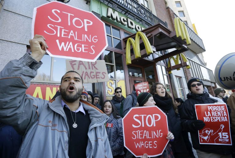 Demonstrator Zev Nicholson, of Boston, left, holds a placard and chants during a protest outside a McDonalds fast foot restaurant, Tuesday, March 18, 2014, in Boston, held to call attention to the denial of overtime pay and other violations protesters say deprive workers of the money they're owed. (AP Photo/Steven Senne)