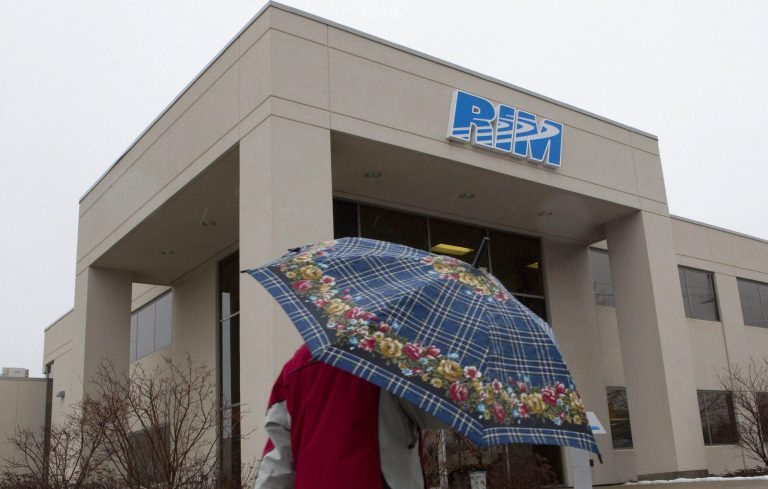   In this Monday, Jan. 23, 2012 photo, a man with an umbrella walks past part of the Research In Motion campus in Waterloo, Ontario, Canada. These are troubling times for Waterloo, the town of 100,000 that was transformed by Research In Motion's BlackBerry into Canada's Silicon Valley. (AP Photo/The Canadian Press, Chris Young)  