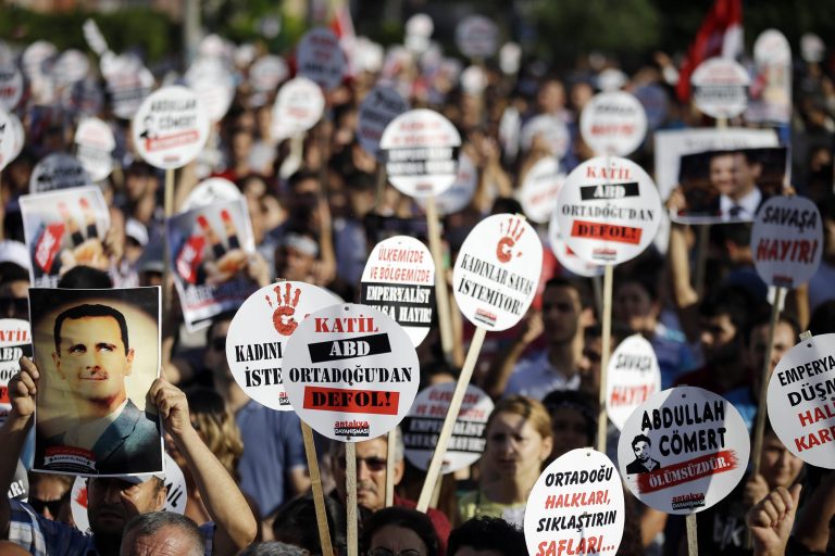 A protesters holds up a poster of Syrian President Bashar Assad near placards reading 