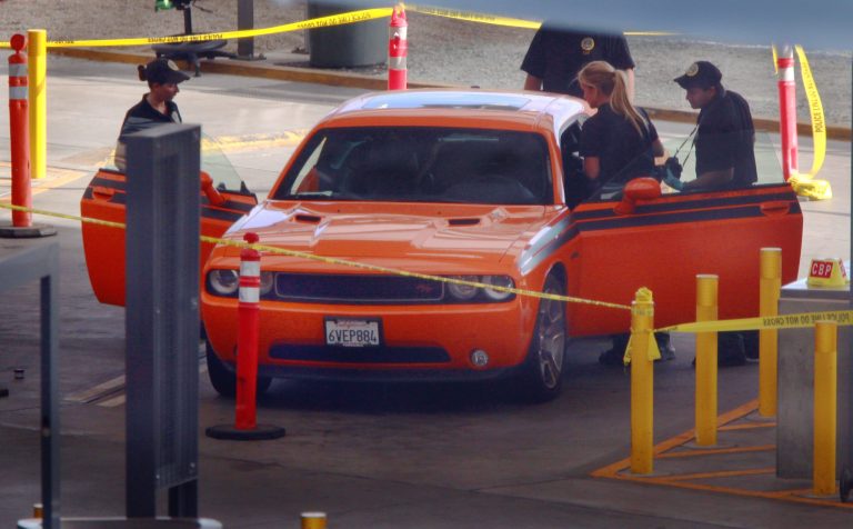 U.S. Customs and Border Protection investigators examine a car in the secondary inspection area at the San Ysidro, Calif., border crossing with Mexico, Tuesday, Aug. 12, 2014. A suspected human smuggling attempt left two men in their 20s dead Tuesday afternoon after they were found in the back of a car that was headed into the United States. Officials would not confirm the orange car was the one the men were found in. (AP Photo/U-T San Diego, John Gastaldo)