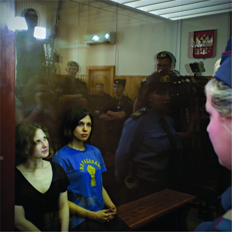 Feminist punk group Pussy Riot members, from left, Maria Alekhina and Nadezhda Tolokonnikova sit in a glass cage at a court room in Moscow, Russia on Friday, Aug. 17, 2012. A judge found three members of the provocative punk band Pussy Riot guilty of hooliganism on Friday, in a case that has drawn widespread international condemnation as an emblem of Russia's intolerance of dissent. T-shirt on right worn by Tolokonnikova is Spanish and translates to 