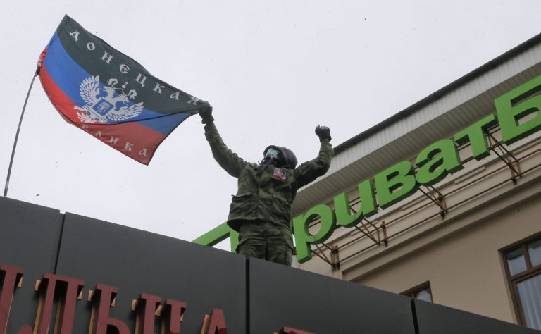 A masked pro-Russian activist places a self-proclaimed 'Donetsk Republic' flag over the office of a 