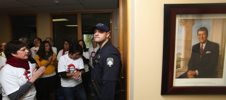 With a picture of President Ronald Reagan and a Bellevue Police officer looking on, Lynne Dodson of the Washington State Labor Council, at left, and others protest for immigration reform Thursday at Washington State Republican Party Headquarters in Bellevue.  (AP Photo/The Seattle Times, Ken Lambert) 