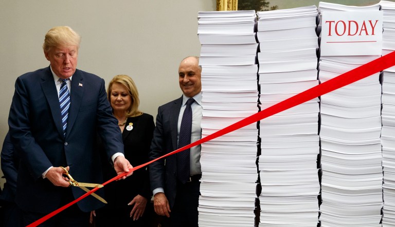 President Trump cut through literal red tape tied to piles of paperwork during an event on deregulation at the White House on Thursday. (AP Photo/Evan Vucci)