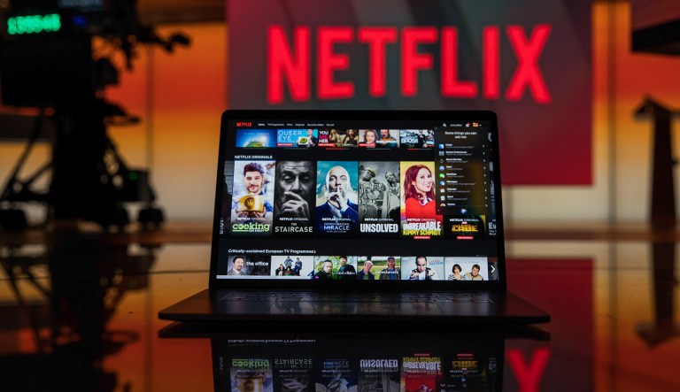 A laptop computer screen displaying the Netflix homepage stands against an illuminated screen bearing the company logo in this arranged photograph in London, U.K., on Tuesday, June 26, 2018. Addressing a room filled with New Delhiâs business elite earlier this year,Â Netflix Inc.Â Chief Executive OfficerÂ Reed HastingsÂ offered a prediction: His companyâs next 100 million customers will come from India.