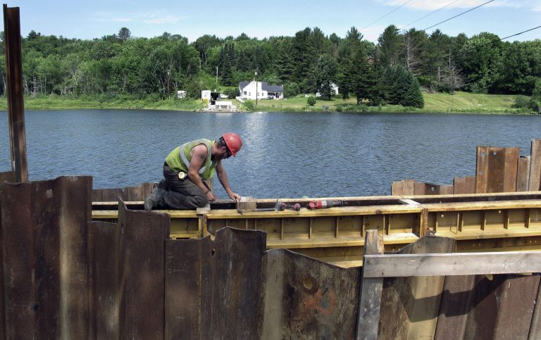 In this July 2, 2014 photo, Forrest Menard works on the first stages of a new floating bridge to carry Route 65 over Sunset Lake in Brookfield, Vt. The state's only floating bridge, originally built in 1820 and listed on the National Register of Historic Places, fell into disrepair, was closed to traffic in 2008 and removed for replacement this year. The new bridge is scheduled to open in May 2015. (AP Photo/Wilson Ring)
