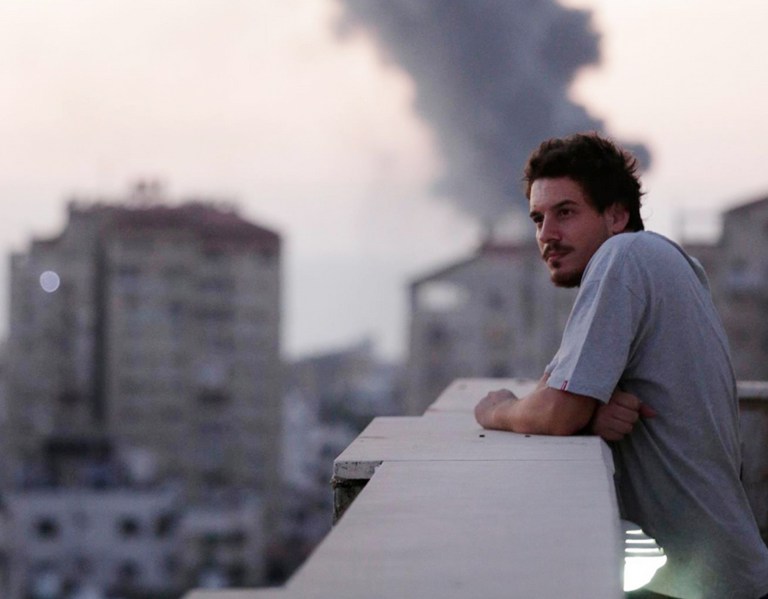 This photo taken in August, 2014 shows Associated Press video journalist Simone Camilli on a balcony overlooking smoke from Israeli Strikes in Gaza City. Camilli, 35, was killed in an ordnance explosion in the Gaza Strip, on Wednesday, Aug. 13, 2014 together with Palestinian translator Ali Shehda Abu Afash and three members of the Gaza police. Police said four other people were seriously injured, including AP photographer Hatem Moussa.(AP Photo/Lefteris Pitarakis)