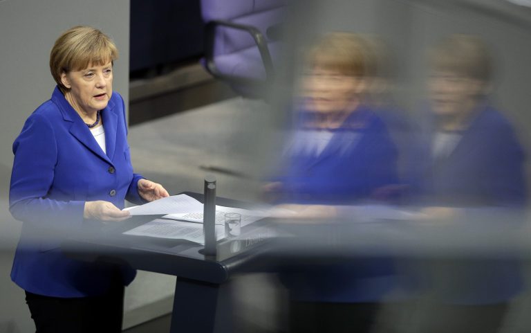 German Chancellor Angela Merkel holds a paper during her speech as part of a meeting of the German federal parliament, Bundestag,  in Berlin, Germany, Thursday, Oct. 16, 2014. The reflections are caused by windows at the visitors tribune. (AP Photo/Michael Sohn)