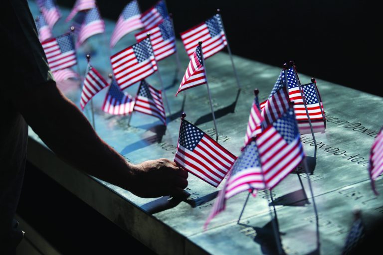 A man fixes an American flag that was fallen from the position during a ceremony marking the 11th anniversary of the Sept. 11 terrorist attacks at the National September 11 Memorial at the World Trade Center site in New York, Tuesday, Sept. 11, 2012. (AP Photo/The New York Times, Chang W. Lee)