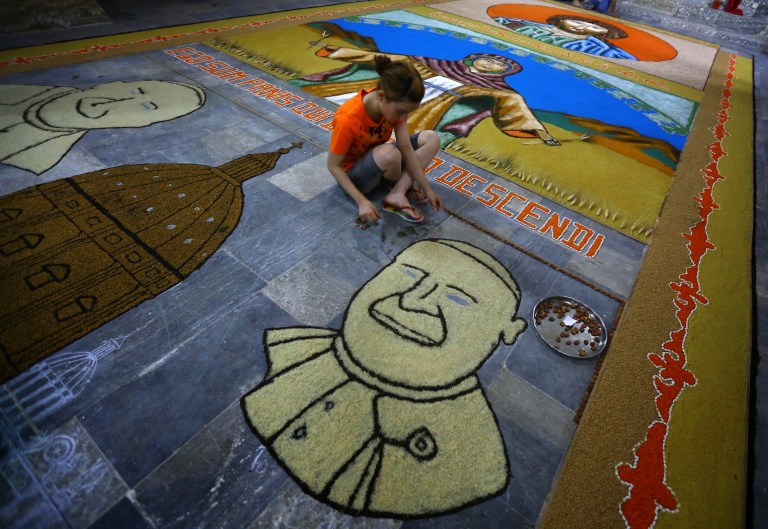 In this Sunday, June 15, 2014 photo, an Iraqi child works on a temporary mosaic of Pope Francis' face made from the area's produce, including wheat, beans and lentils to commemorate an upcoming harvest feast, at the Chaldean Church of the Virgin Mary of the Harvest, in Alqosh, a village of some 6,000 inhabitants about 50 kilometers (31 miles) north of Mosul, northern Iraq. Dozens of Christian families that fled to this ancient Iraqi village have taken a much-traversed route -- many from their minority community have escaped to Alqosh before, in fear for their lives. This time, few say they want to go back to their homes, seeking safety under the Kurdish forces known as the peshmerga. (AP Photo)