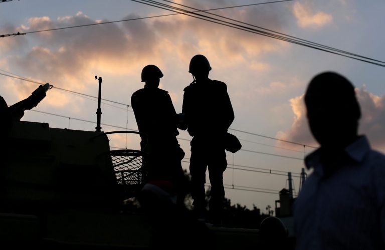   Egyptian army soldiers stand on top of their tank as the sun sets outside the presidential palace, background, in Cairo, Egypt, Saturday, Dec. 8, 2012. Egypt's military warned Saturday of 'disastrous consequences' if the crisis that sent tens of thousands of protesters back into the streets is not resolved, signaling the army's return to an increasingly polarized and violent political scene.(AP Photo/Hassan Ammar)  