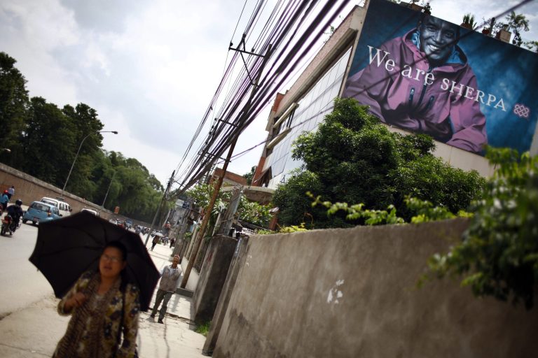 **TO GO WITH STORY SLUGGED NEPAL SHERPAS BY BINAJ GURUBACHARYA** In this Thursday, June 19, 2014, photo, a Nepalese woman walks past a big banner of Sherpa in Katmandu, Nepal. The deadliest disaster in Everest history _an avalanche that swept 16 Sherpas to their death in April as they ferried clients' equipment up the mountain, have finally shaken most of them, now, more and more Sherpas have decided that the dangers of their chosen profession outweigh the financial advantages. (AP Photo/Niranjan Shrestha)