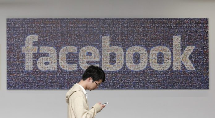 In this June 11, 2014 photo, a man walks past a Facebook sign in an office on the Facebook campus in Menlo Park, Calif. British data protection authorities said Wednesday, July 2, that it is investigating revelations that Facebook conducted a psychological experiment on its users.