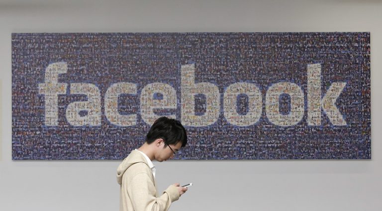 In this June 11, 2014 photo, a man walks past a Facebook sign in an office on the Facebook campus in Menlo Park, Calif. British data protection authorities said Wednesday, July 2, that it is investigating revelations that Facebook conducted a psychological experiment on its users.