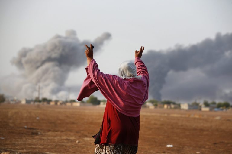 Syrian Kurd Kiymet Ergun, 56, gestures,  in Mursitpinar on the outskirts of Suruc, at the Turkey-Syria border, as thick smoke rises following an airstrike by the US-led coalition in Kobani, Syria as fighting continued between Syrian Kurds and the militants of Islamic State group, Monday, Oct. 13, 2014. Kobani, also known as Ayn Arab, and its surrounding areas, has been under assault by extremists of the Islamic State group since mid-September and is being defended by Kurdish fighters. (AP Photo/Lefteris Pitarakis)