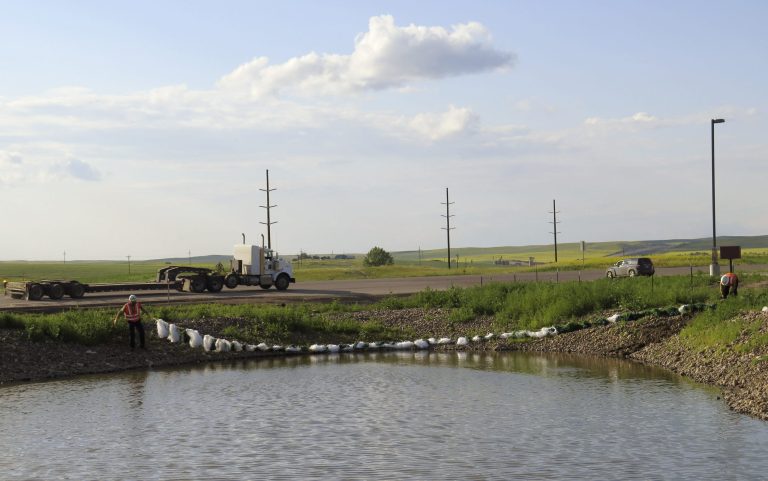 In this Monday, July 7, 2014 photo, cleanup workers deploy booms along the edge of a small reservoir at the site of a saltwater disposal facility that was struck by a lightning strike near Alexander, N.D. The strike at the facility sparked a fire and the release of 2,813 barrels of saltwater and 649 barrels of oil.  (AP Photo/Josh Wood)