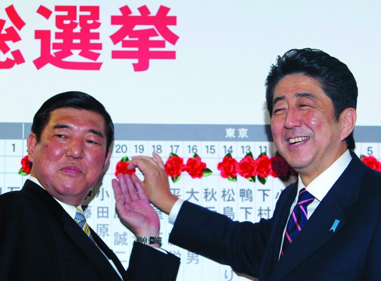 Japan's main opposition leader Shinzo Abe, right, of the Liberal Democratic Party, and the party Secretary-General Shigeru Ishiba pose for photos as they place a rosette on the name of one of those elected in parliamentary elections at the party headquarters in Tokyo Sunday, Dec. 16, 2012. Japan's conservative LDP stormed back to power Sunday after three years in opposition, exit polls showed, signaling a rightward shift in the government that could further heighten tensions with rival China. (AP Photo/Junji Kurokawa)