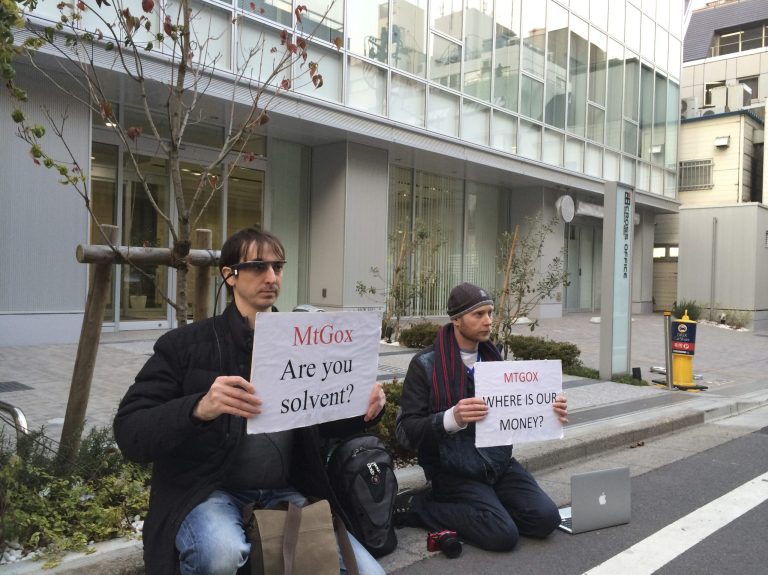Bitcoin trader Kolin Burges, right, of London and American Aaron (only his first name was given) hold protest signs as they conduct a sit-in in front of the office tower housing Mt. Gox in Tokyo Tuesday. (AP/Kaori Hitomi)