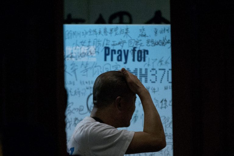 One of the relatives of Chinese passengers on board Malaysia Airlines Flight 370 rubs his head near a board covered with written wishes from relatives during a briefing given by Malaysian officials at a hotel in Beijing, China, Wednesday, March 26, 2014. Some of the wishes, partially seen, read, 