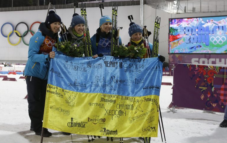 Ukraine's relay team Vita Semerenko, Juliya Dzhyma,  Olena Pidhrushna and Valj Semerenko, from left, celebrate with Ukrainian flag with writings on it after winning the gold during the flower ceremony of the women's biathlon 4x6k relay at the 2014 Winter Olympics, Friday, Feb. 21, 2014, in Krasnaya Polyana, Russia. (AP Photo/Kirsty Wigglesworth)