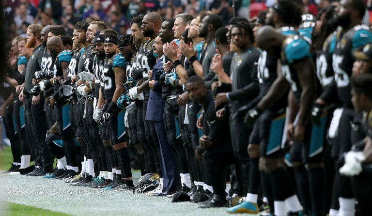 Jacksonville Jaguars owner Shahid Khan, center, joins arms with players as some kneel down during the playing of the U.S. national anthem before an NFL football game against the Baltimore Ravens at Wembley Stadium in London, Sunday Sept. 24, 2017. (AP Photo/Tim Ireland)