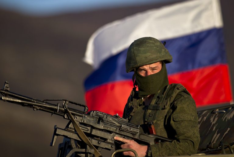 A soldier is backdropped by a Russian flag while manning a machine gun outside a military base in Perevalne, Ukraine, Saturday, March 15, 2014. (AP Photo/Vadim Ghirda)