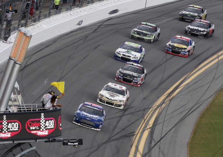 Aric Almirola, front, leads the NASCAR Sprint cup Series auto race ahead of Brian Vickers and other as he passes the flag stand with a caution flag at Daytona International Speedway in Daytona Beach, Fla., Sunday, July 6, 2014.  Moments later the race was stopped because of rain and Almirola was announced the winner.  (AP Photo/David Graham)