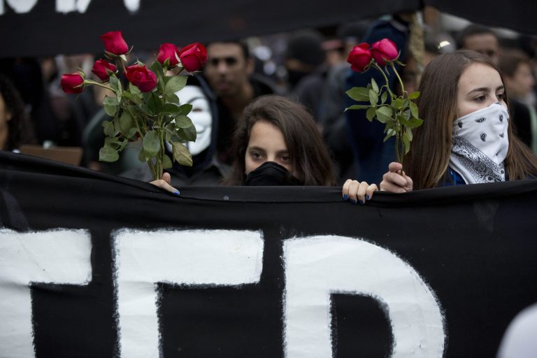Masked protesters carry a banner and roses while marching in Sao Paulo, Brazil, Thursday, June 19, 2014. The protest in Sao Paulo, Brazil's biggest city that is hosting a World Cup match,  was called by the Free Fare movement, the group that was behind the first protests last year that sparked roiling anti-government demonstrations across Brazil. (AP Photo/Eduardo Verdugo)