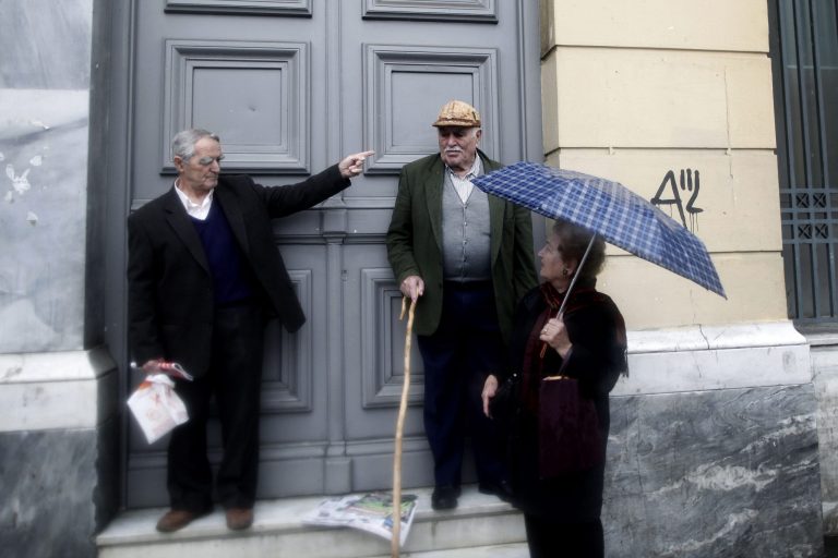   Athenians chat outside a bank as they shelter from a rainfall in central Athens, Tuesday, Dec. 18, 2012. Greece is failing to collect the tax it is owed and is in danger of missing key targets that need to be met to reduce the government's staggering debt pile, the European Union warned on Monday. (AP Photo/Petros Giannakouris)  