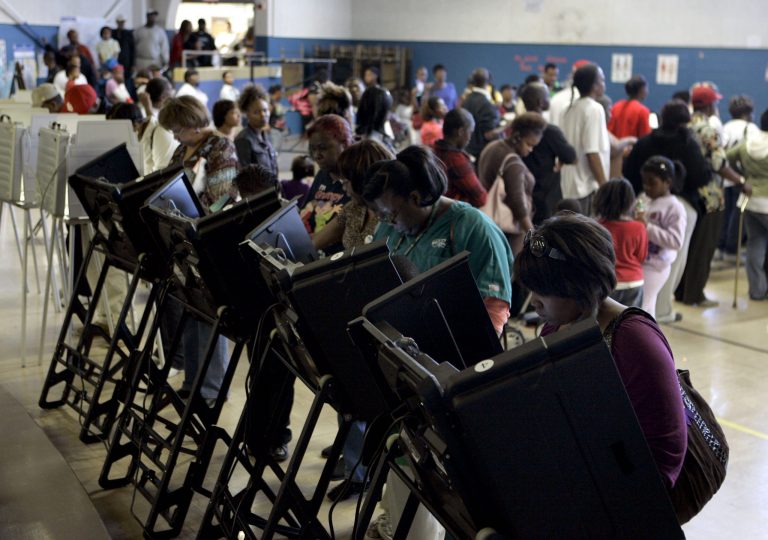 Voters cast their ballots in a school gymnasium as others wait in line in the background Tuesday, Nov. 4, 2008, in Ferguson, Mo. Voters waited in line for hours at the location in order to cast their ballot. (AP Photo/Jeff Roberson)