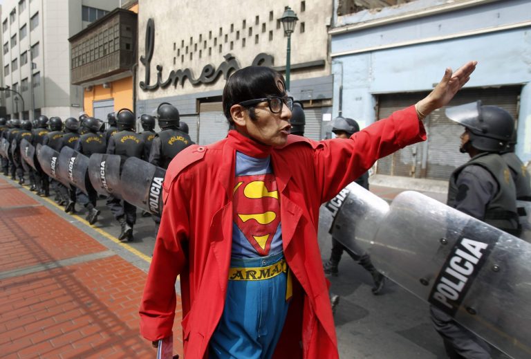   In this photo taken June 13, 2012, Avelino Chavez, wearing his signature Superman costume, waves and greets riot police walking in formation toward a plaza where a protest is expected to take place in downtown Lima, Peru. Chavez, 52, took on the Superman persona 15 years ago, when he lost his job as a security guard, and says he has had work ever since. Chavez also says he only earns about $160 US dollars per month, but that he has the strength of a superhero. Chavez currently works to promote a travel agency. (AP Photo/Martin Mejia)  