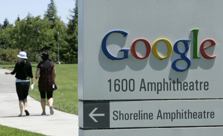 Two women walk past a Google sign at the Google campus in Mountain View, Calif.