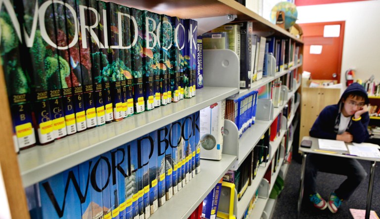 A student studies in a high school library near a series of encyclopedia books.