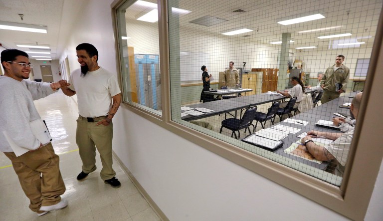 In this photo taken Thursday, Jan. 28, 2016, Rudy Madrigal, left, shares a fist bump with fellow inmate Nicolas Melendrez before Madrigal headed into his world history classroom, at right, at the Monroe Correctional Complex in Monroe, Wash.