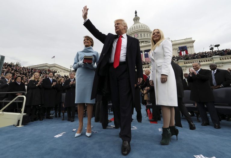 President Trump waves after taking the oath of office as his wife Melania holds the Bible, and Tiffany Trump looks out to the crowd.