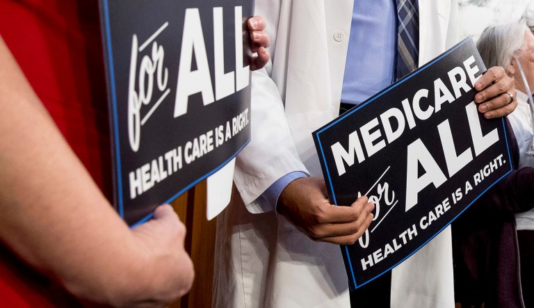 Two people hold signs supporting "Medicare for All" in D.C.