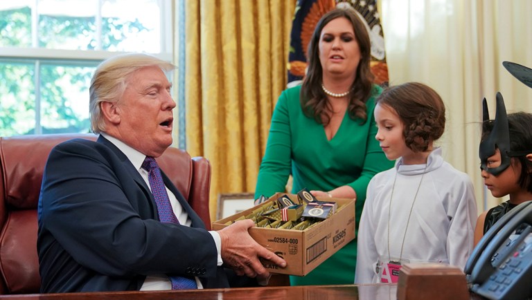 President Donald Trump is handed a box of candy by White House press secretary Sarah Huckabee Sanders, center, to pass out to children dressed in their Halloween costumes.