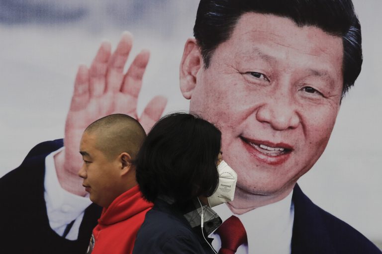 Pedestrians, one wearing a mask, walk by a poster of Chinese President Xi Jinping on a street in Beijing.