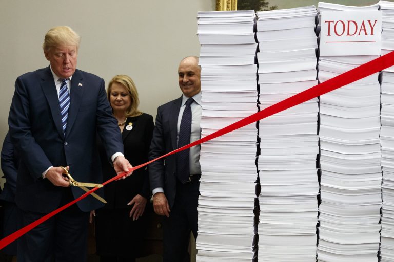 President Donald Trump cuts a ribbon during an event on federal regulations in the Roosevelt Room of the White House, Thursday, Dec. 14, 2017, in Washington. "Let's cut the red tape, let's set free our dreams," Trump said as he symbolically cut a ribbon on stacks of paper representing the size of the regulatory code.