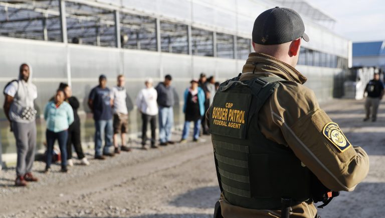 Government agents stand guard alongside suspects taken into custody during an immigration sting at Corso's Flower and Garden Center, Tuesday, June 5, 2018, in Castalia, Ohio. The operation is one of the largest against employers in recent years on allegations of violating immigration laws.