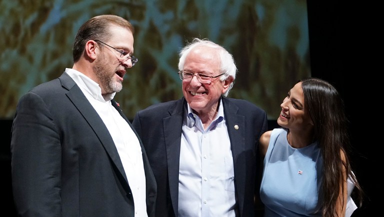 Kansas congressional candidate James Thompson, left, Sen. Bernie Sanders, I-Vt.,  and Alexandria Ocasio-Cortez, a Democratic congressional candidate from New York, stand together on stage after a rally.