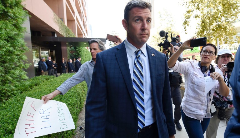 U.S. Rep. Duncan Hunter, center, leaves an arraignment hearing as a protester carries a sign, left, Thursday, Aug. 23, 2018, in San Diego. Hunter and his wife Margaret pleaded not guilty Thursday to charges they illegally used his campaign account for personal expenses. 