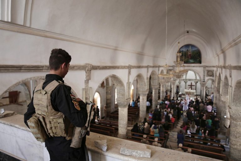 In this April 16, 2017, photo a Christian militiaman stands guard during Easter mass in Qaraqosh, Iraq. Synagogues, mosques, churches and other houses of worship are routinely at risk of attack in many parts of the world. And so worshippers themselves often feel the need for visible, tangible protection even as they seek the divine.
