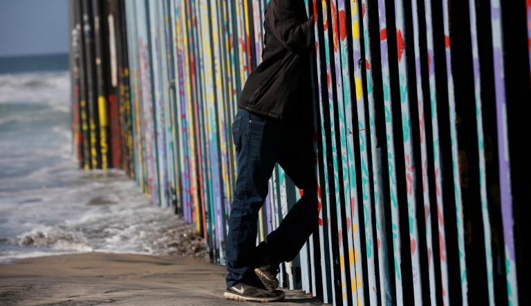 A man looks through the U.S. border wall into San Diego, California from the beach in Tijuana, Mexico, Tuesday, Dec. 11, 2018.