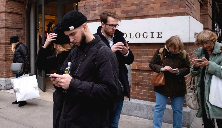 People using mobile phones stand next to Chelsea Market in New York.