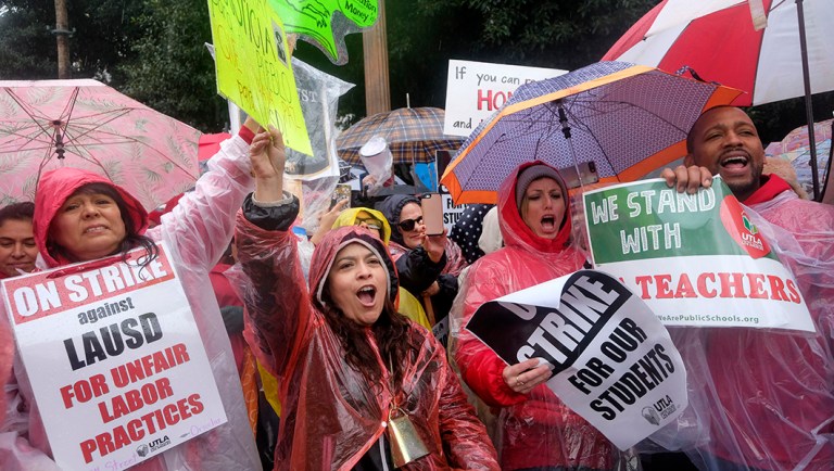 Teachers and supporters hold signs in the rain during a rally.