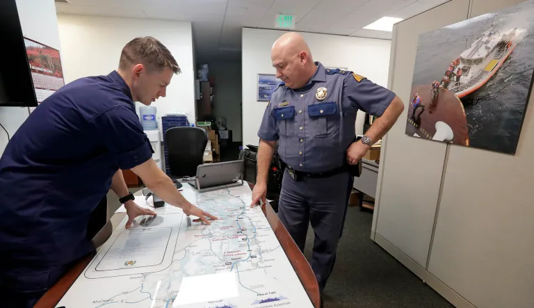 U.S. Coast Guard Lt. Cmdr. Blair Sweigert, left, who missed a paycheck a day earlier during the partial government shutdown, works with Washington State Patrol Capt. Dan Atchison in a shared office where they coordinate marine security at Sector Puget Sound base Wednesday, Jan. 16, 2019, in Seattle. The Coast Guard is part of the U.S. Department of Homeland Security, which is unfunded during the shutdown, now in its fourth week.